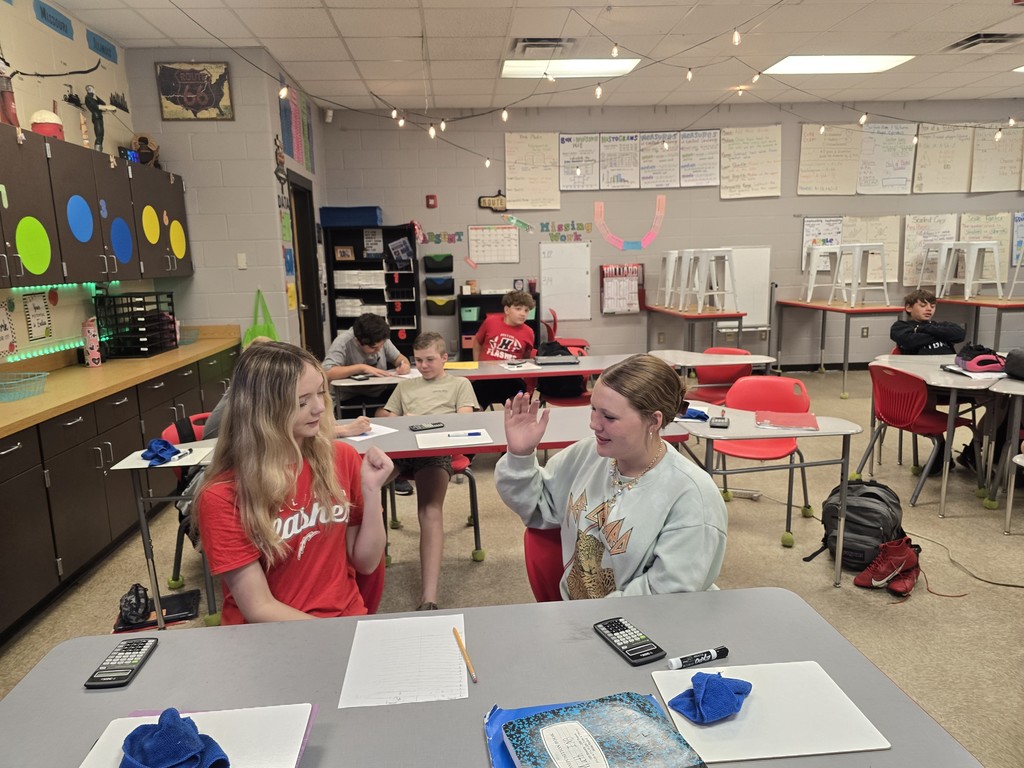Students at desk playing rock, paper, scissors.