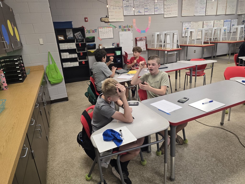 Students at desk playing rock, paper, scissors.