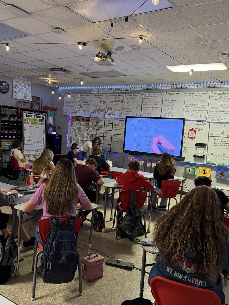 Teacher giving instruction while students take notes.