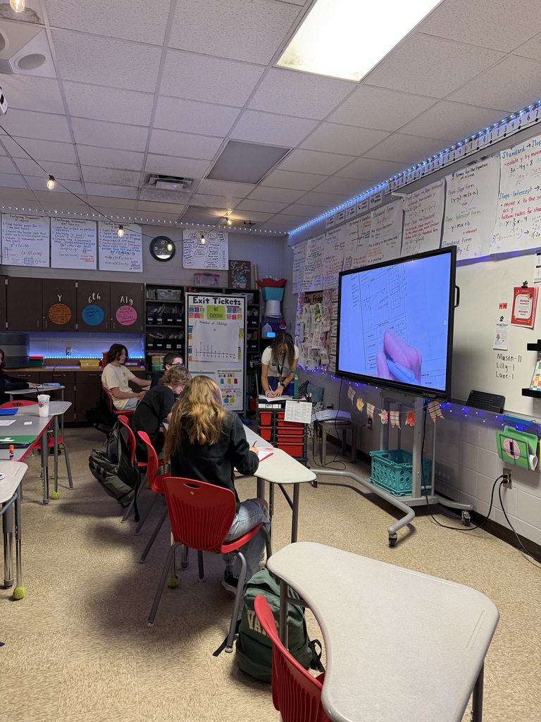 Teacher giving instruction while students take notes.