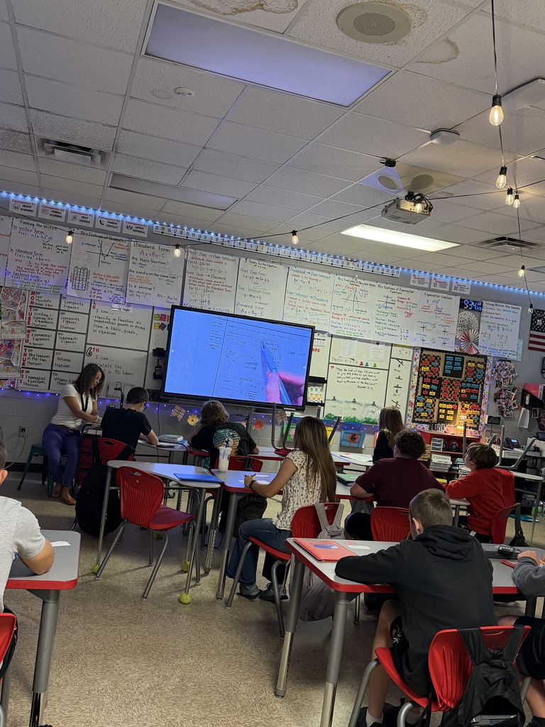 Teacher giving instruction while students take notes.