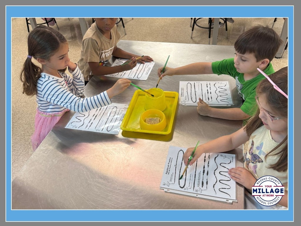Four elementary students sitting at a classroom table working on art projects with paint and paper. A "Millage at Work" logo is visible in the bottom right corner of the image.
