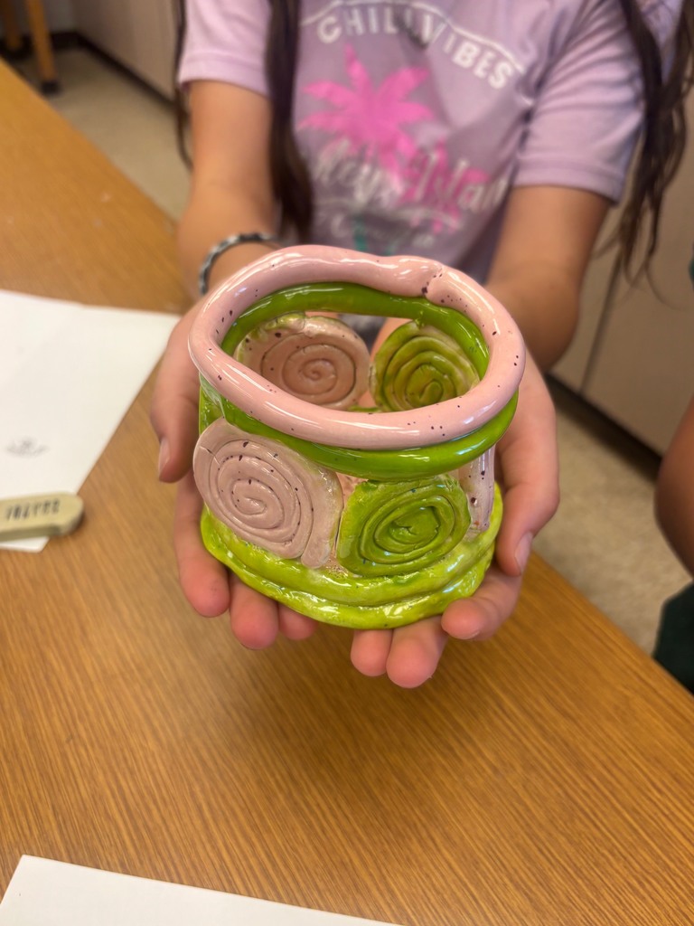 A close up picture of a clay bowl that is pink and green. The outside walls are lines with pink and green swirls. A student is holding it in her hands.