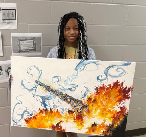 Female student smiles for the camera as she holds her own painting, a large canvas with a saxophone that is expelling flames surrounded by smoke. 
