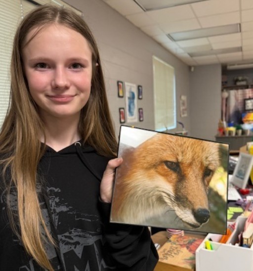 Student smiles for the camera holding a photograph she took of a fox. The photo is an up close shot and framed around the animal's face. 