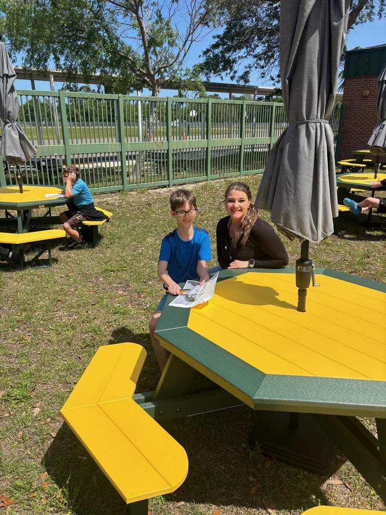Ms. Perry and her student pose for a picture at YMS green and gold picnic table outside on campus. 
