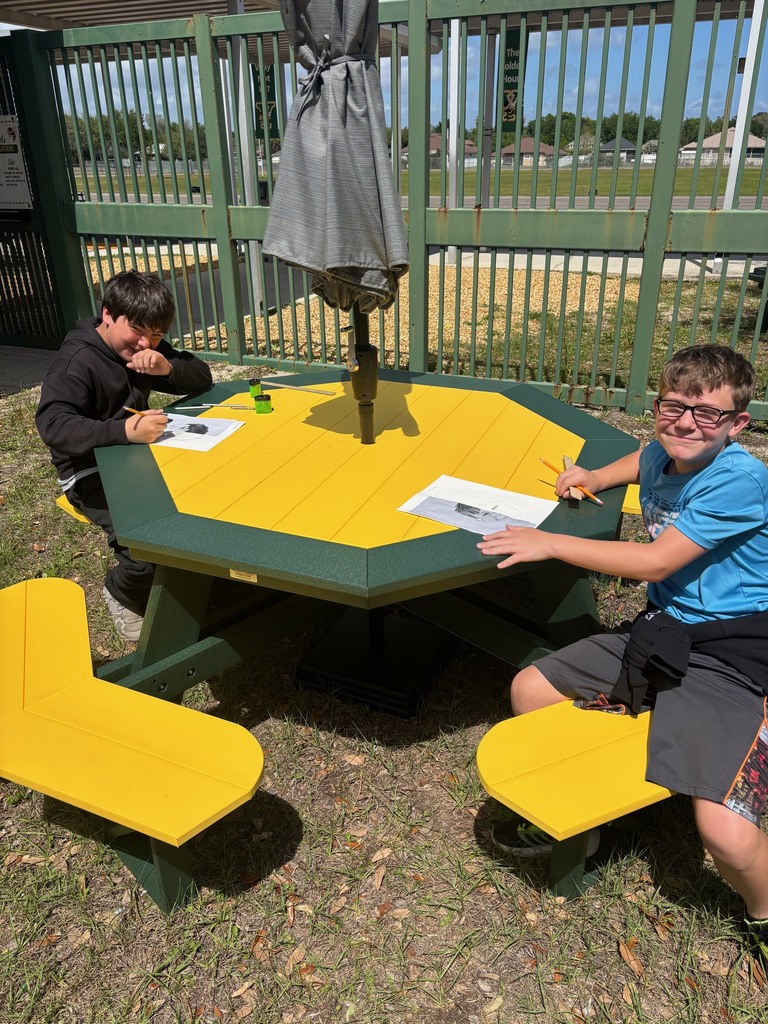 Two students smile for the camera as they work on their art projects at the new green and gold picnic tables.