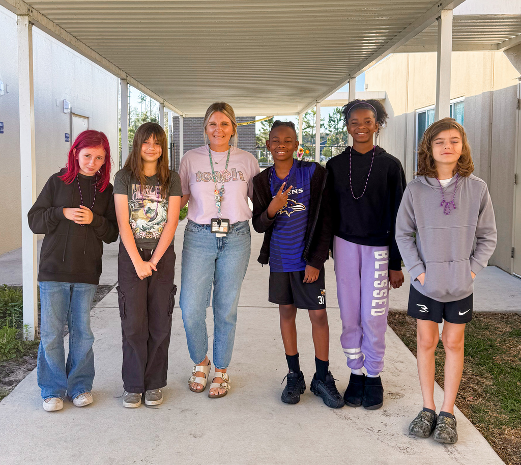 A teacher and five students standing together under a covered school walkway. They are all wearing purple shirts and smiling for the camera to celebrate Military Child Appreciation Day.