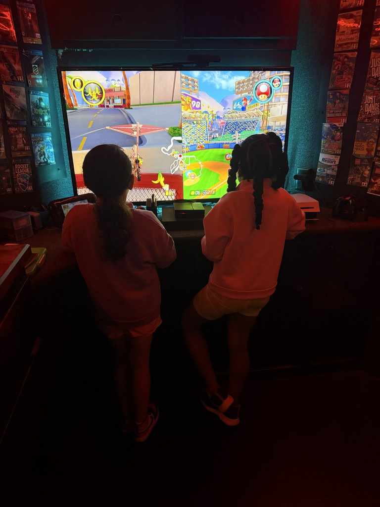 Close-up of a high-definition television screen inside a dark gaming trailer, showing a vibrant video game menu under bright green neon accent lighting.