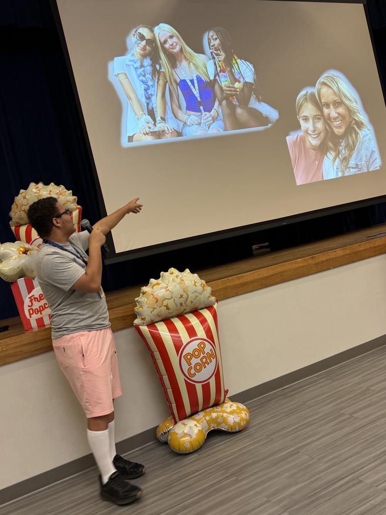 Student speaking on a microphone and pointing to pictres on a screen behind him. 