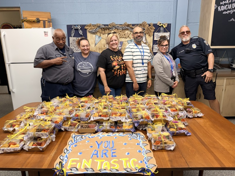 A group of adults standing behind a table full of boxes of treats for the ELH staff 