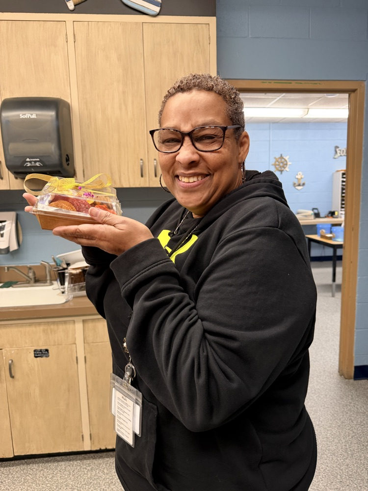 A woman smiling and holding up a box full of meat, crackers, cheese, olives and dried fruit 