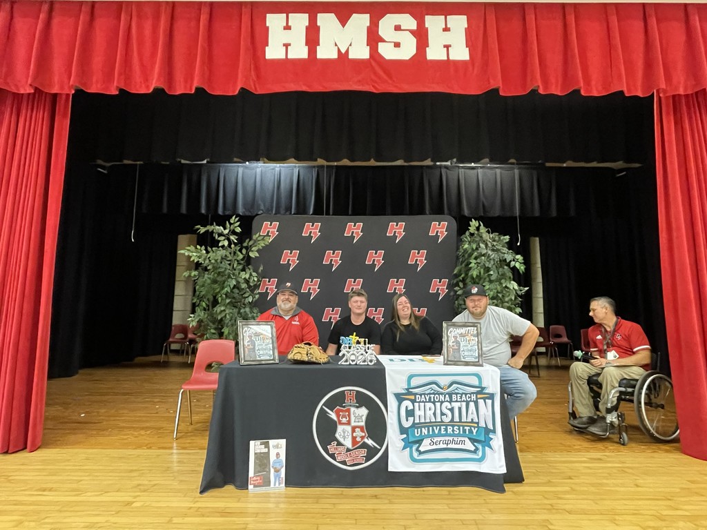 Student posing with coach and family at signing table.