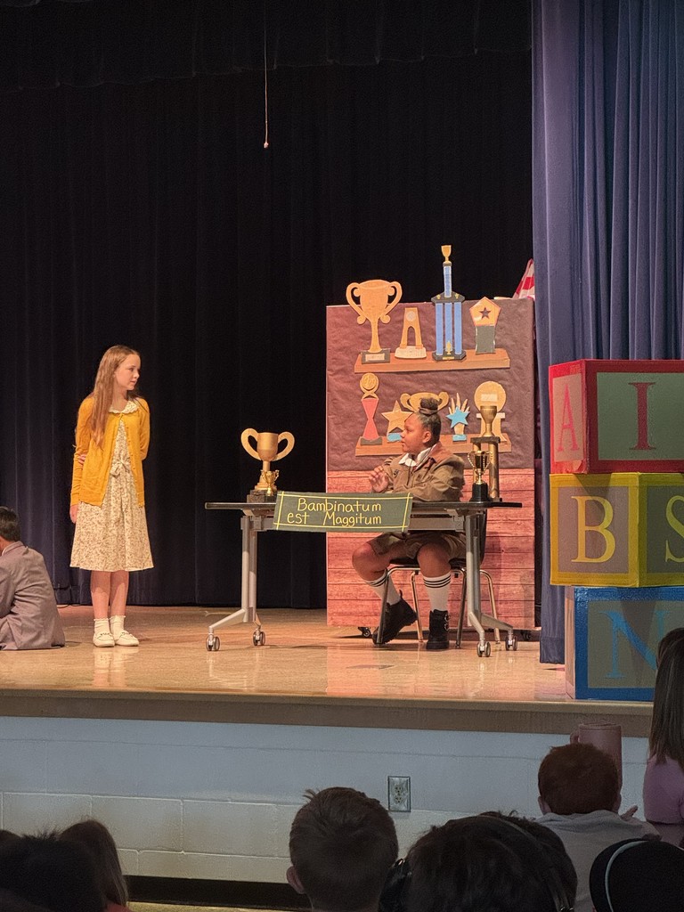 A close-up shot of two lead characters talking on stage, framed by the dark theater curtains and stage lighting.