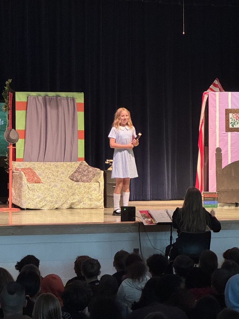 A solo performer or small group stands near a tall, colorful set flat painted with geometric patterns and bright colors.