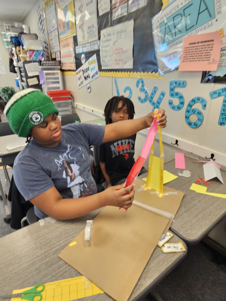 A group of students gathered around a desk, excitedly discussing and testing a collaborative building project.