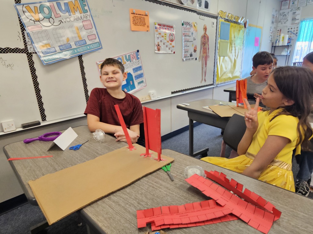 A student smiles while working on a creative design project, surrounded by various art and building supplies.