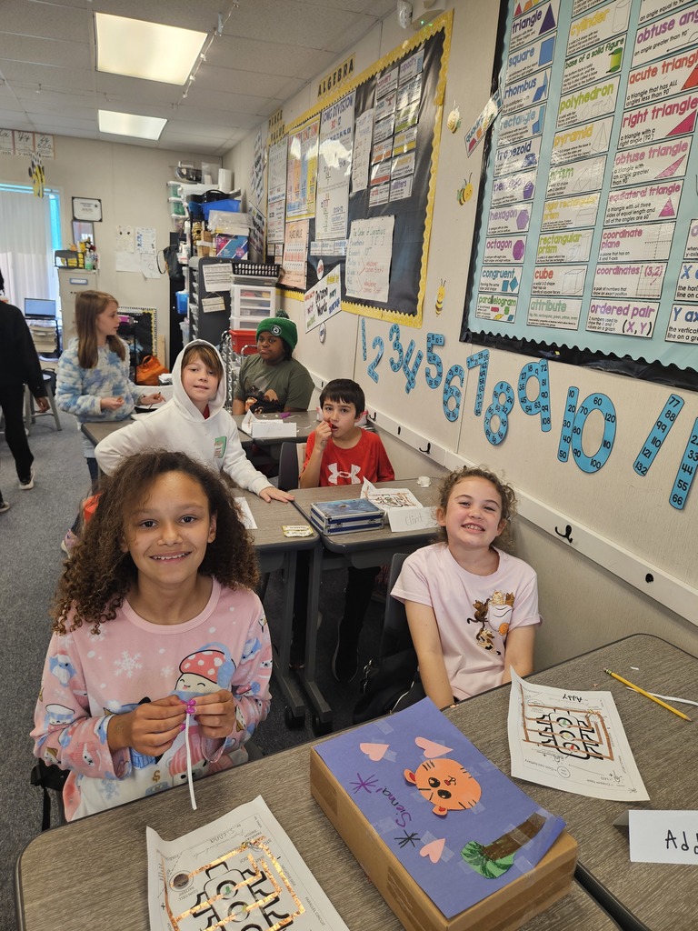Three students smiling and posing together behind their completed STEM project at a classroom table.