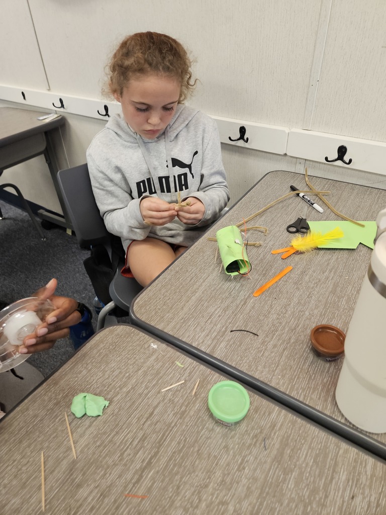 A close-up shot of a student's hands carefully adjusting a marble run structure made of recycled materials and green plastic tubing.