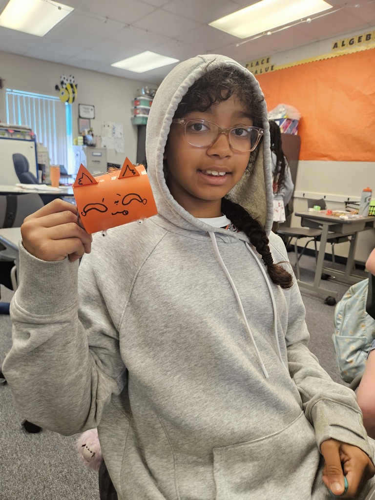 A student smiles while working on a creative design project, surrounded by various art and building supplies.