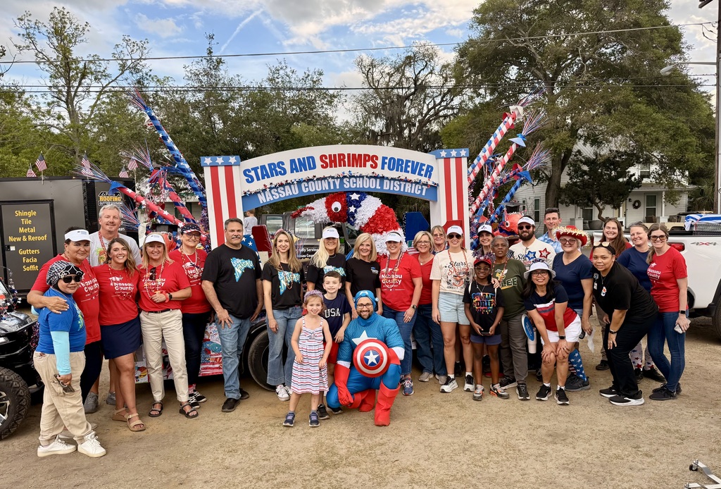 A large group of Nassau County School District staff, students, and families pose together in front of the decorated parade float.