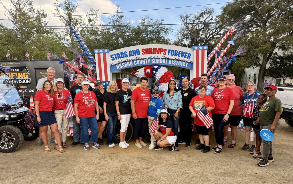 A large group of Nassau County School District staff, students, and families pose together in front of the decorated parade float.