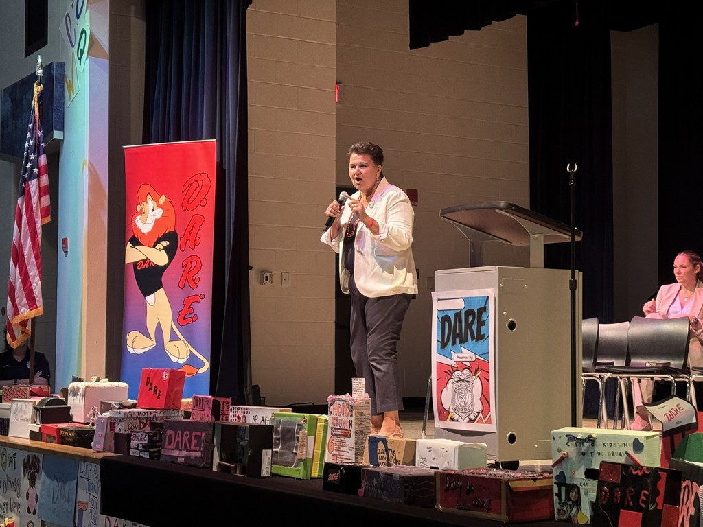 Dr. Burns speaking at the podium on stage, addressing the 5th-grade students and their families about the importance of making positive choices.