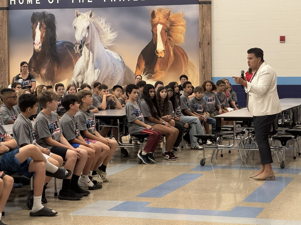 A wide shot of the 5th-grade class seated in the auditorium during the D.A.R.E. graduation ceremony, with the stage visible in the background decorated for the event.