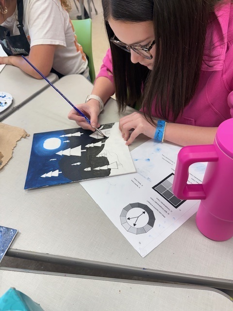 One student works on the final touches to her color scheme painting. Pink Stanley type cup sits on the table beside her work. 