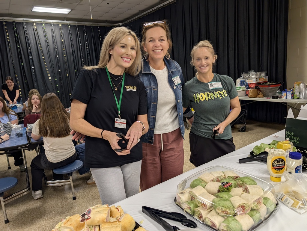 Three volunteers smile for the camera as they help serve publix subs and wraps to teachers and staff. 
