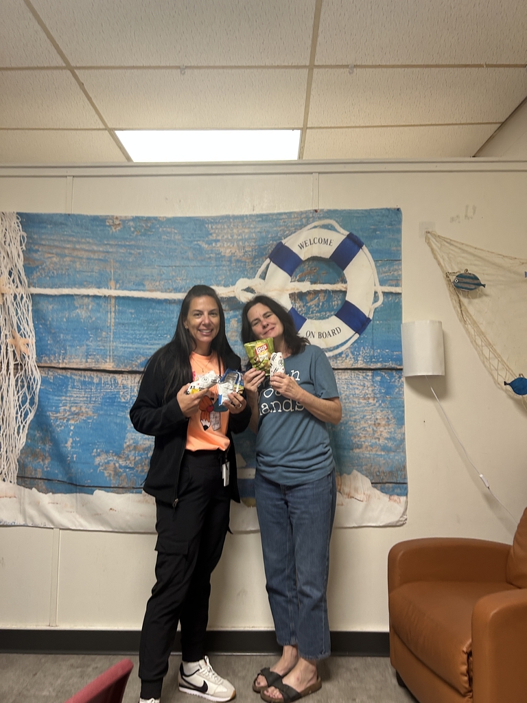 Two staff members posing in front of a teal nautical background holding their sandwiches and chips.