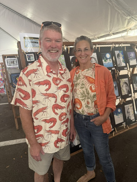 A teacher and her husband smile for the camera as they are checking out the student art exhibit.