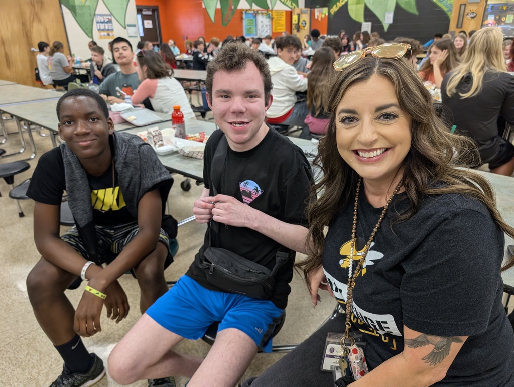 Female teacher smiles for the camera with two male students at the lunch table. 