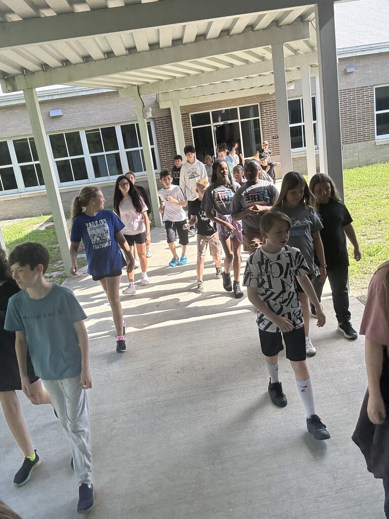 Elementary school students enthusiastically raising their hands and cheering from the side of a school hallway.