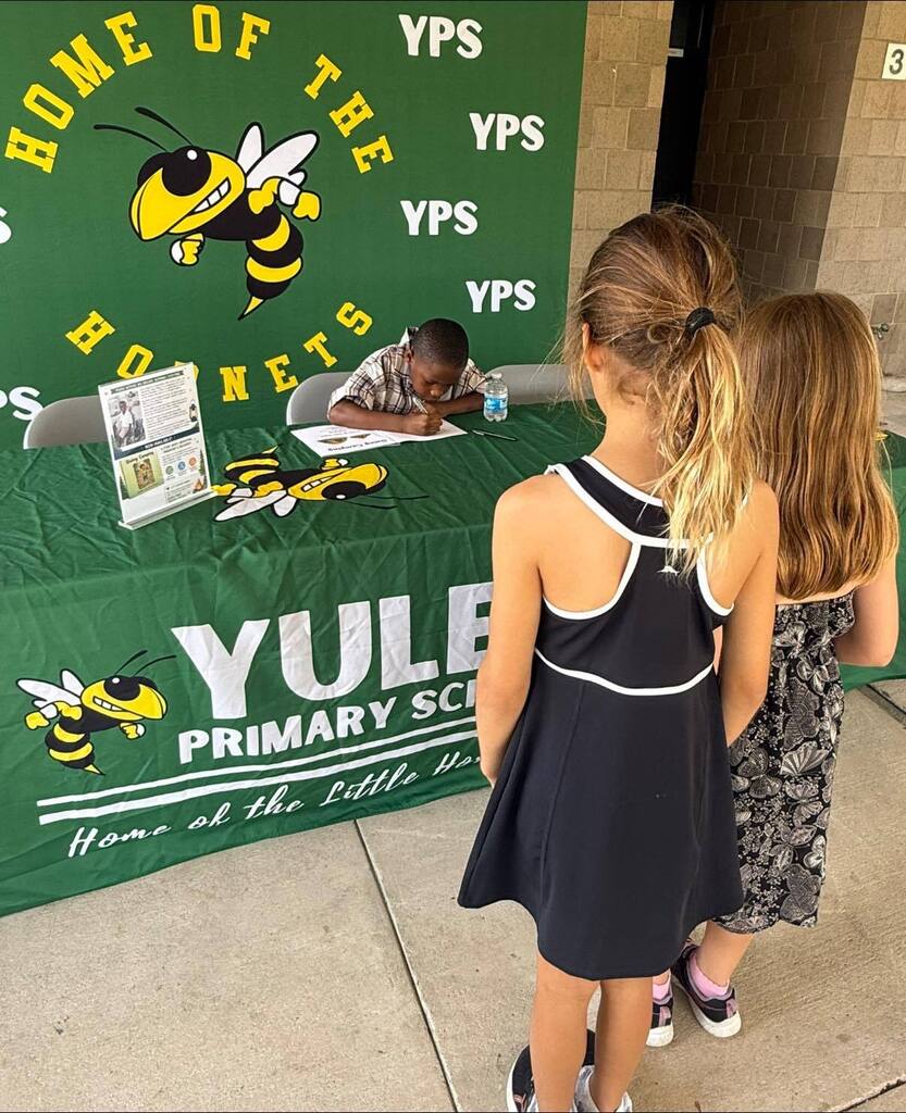 Two students wait in line while first grade student author Amari signs copies of his book Going Camping at a Yulee Primary School book signing event.
