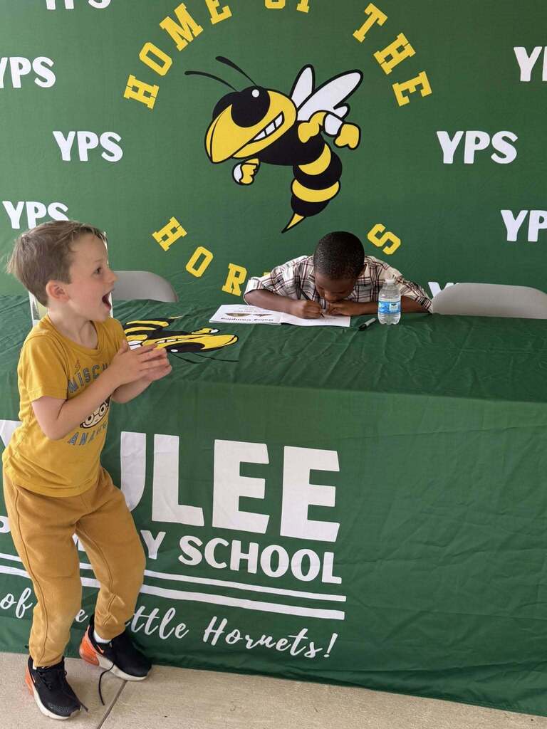 A student reacts excitedly while first grade student author Amari signs a copy of Going Camping at a Yulee Primary School book signing event.