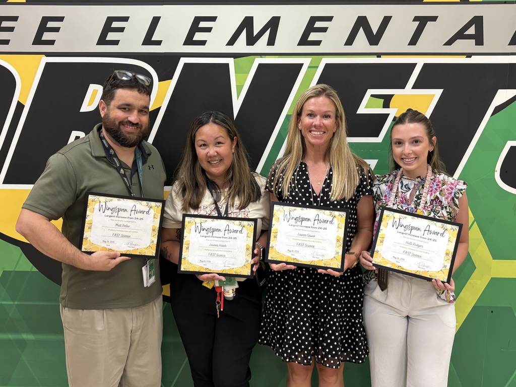 A group photo of Yulee Elementary teachers and staff smiling and holding certificates in front of a green and yellow wall featuring the school's "Hornets" logo and mascot.