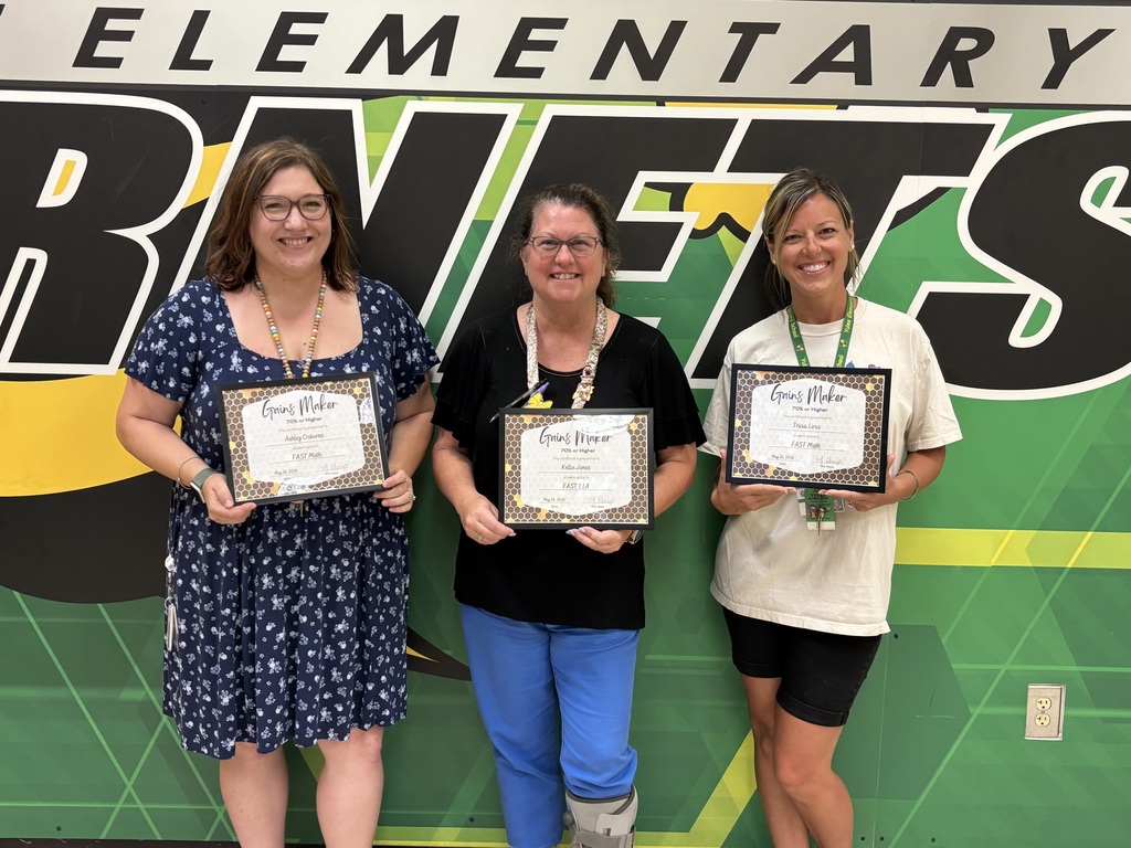 A group photo of Yulee Elementary teachers and staff smiling and holding certificates in front of a green and yellow wall featuring the school's "Hornets" logo and mascot.