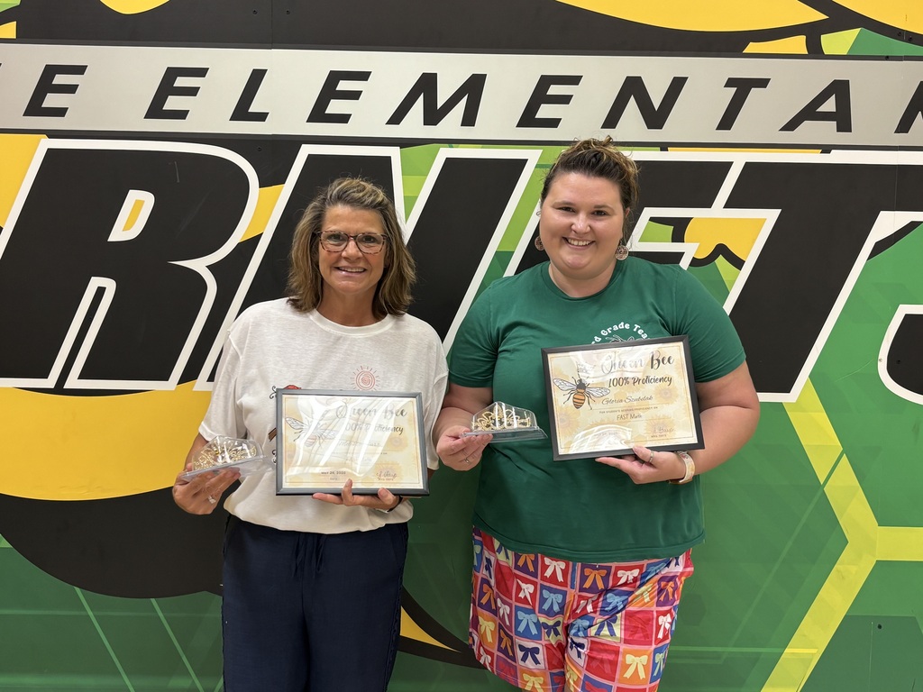 A group photo of Yulee Elementary teachers and staff smiling and holding certificates in front of a green and yellow wall featuring the school's "Hornets" logo and mascot.