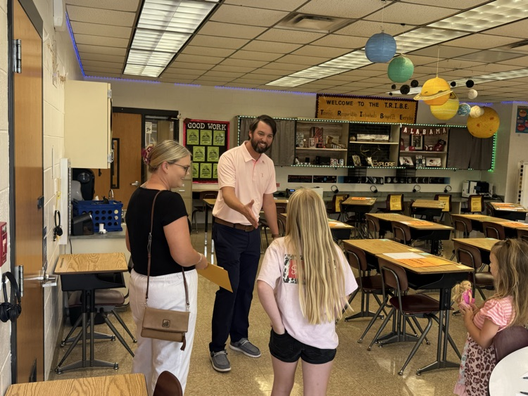 Mr. Griffis greets a student and her family with a handshake as they arrive for a back-to-school meet-and-greet in his classroom. 