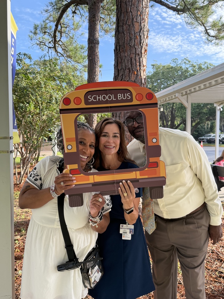 Three people holding a school bus frame and posing for a picture in front of trees.
