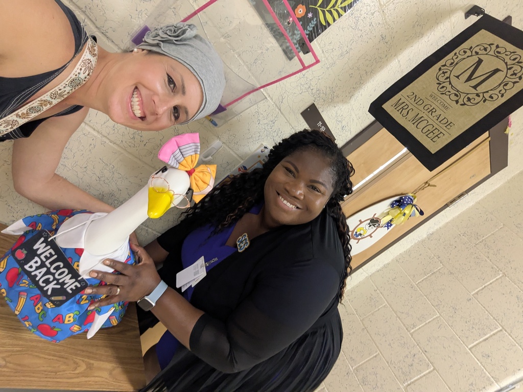 Two adults pose for a selfie with a front porch goose dressed in a back to school outfit with a pencil bow.