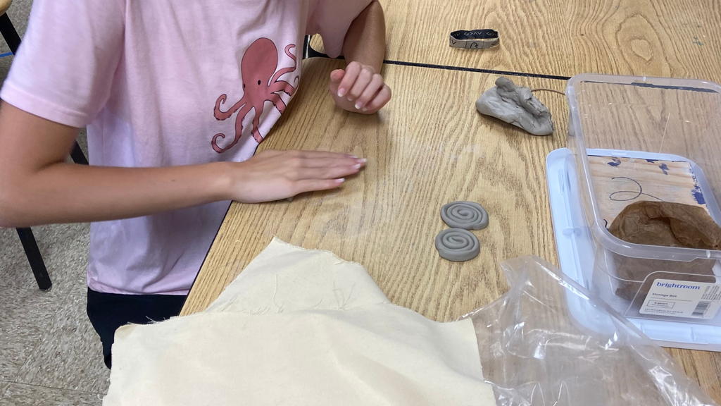 Student making coils with clay on a wooden table.