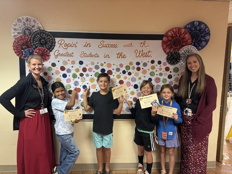 Five students proudly display their Warrior Praise certificates while standing with two teachers in front of a colorful Western-themed bulletin board. The group celebrates student success and positive achievements at school.