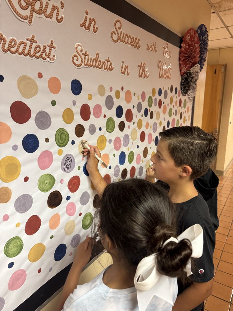 Students add their own creative drawings to a colorful collaborative bulletin board filled with painted circles. Working together, they transform the display into a celebration of student creativity, individuality, and school community.
