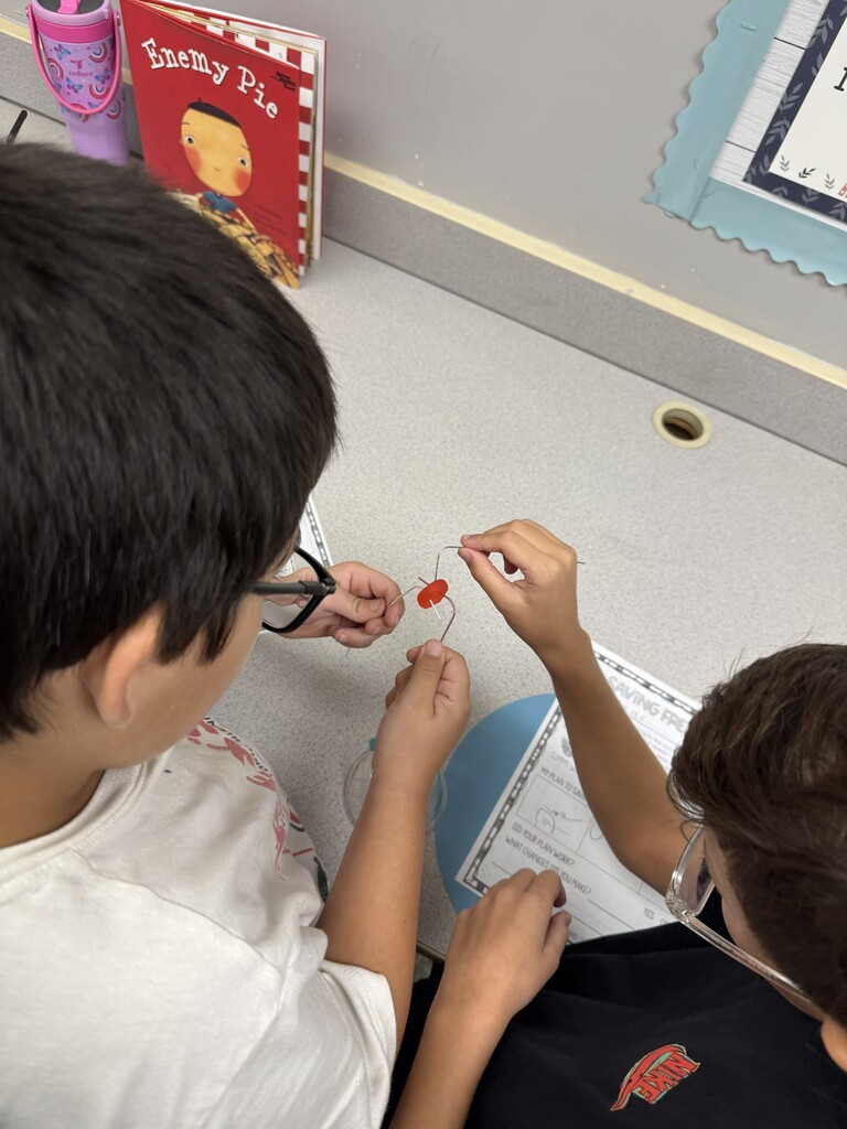 Students work to use a paperclip to pull a gummy worm through a life saver.