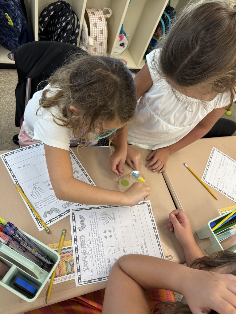 Students work to use a paperclip to pull a gummy worm through a life saver.