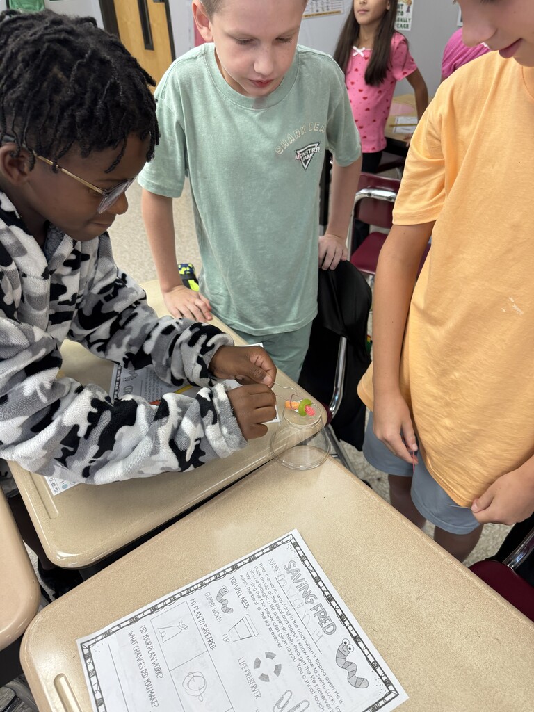 Students work to use a paperclip to pull a gummy worm through a life saver.