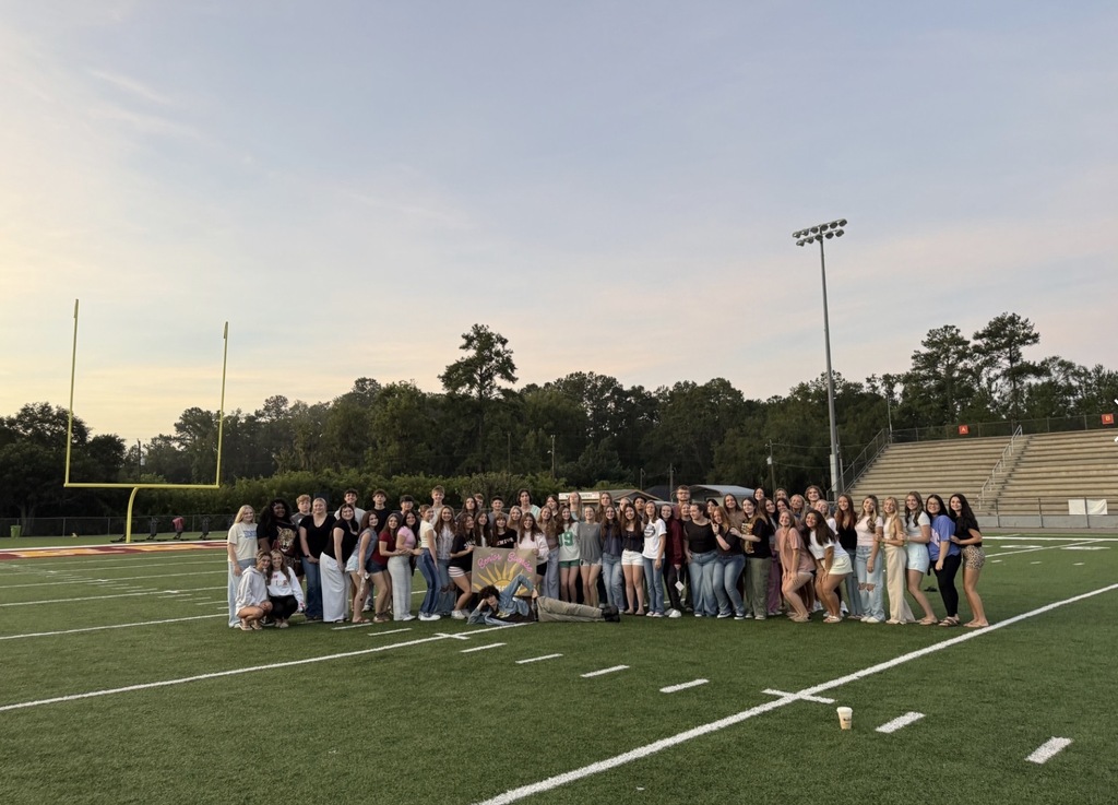 Three photos show a large group of West Nassau High School students gathered on the football field during an evening senior sunrise event. In the first photo, students pose together near the end zone as the sky begins to brighten. In the second and third photos, students sit together on blankets at midfield facing the sunrise, with the stadium, goalposts, and school buildings visible in the background