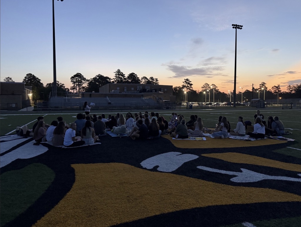 Three photos show a large group of West Nassau High School students gathered on the football field during an evening senior sunrise event. In the first photo, students pose together near the end zone as the sky begins to brighten. In the second and third photos, students sit together on blankets at midfield facing the sunrise, with the stadium, goalposts, and school buildings visible in the background